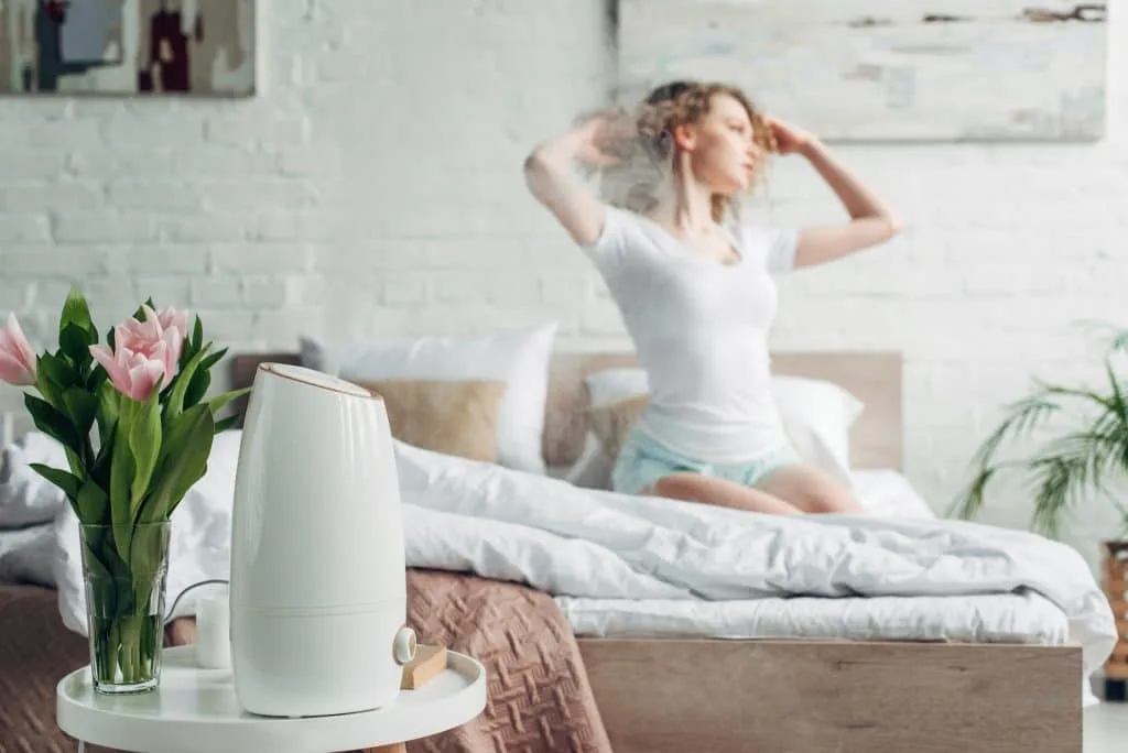 selective focus of girl sitting in bedroom with tulip flowers and air purifier spreading steam