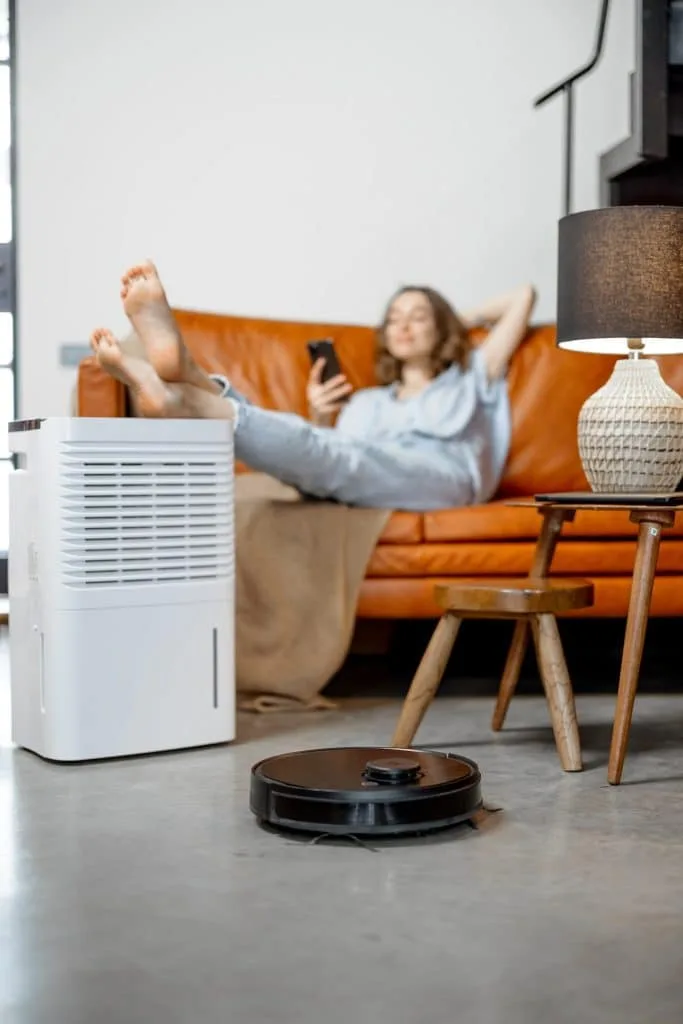 Woman sitting near air purifier and robotic vacuum cleaner